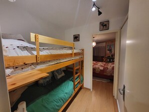 Ein Zimmer mit Etagenbetten, einem Holztisch und einer Tür zu einem anderen Raum.