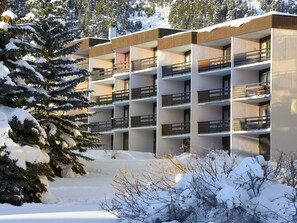 Ein mehrgeschossiges Gebäude mit Balkonen, umgeben von schneebedeckten Bäumen und Sträuchern.
