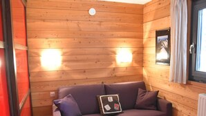 A wooden cabin interior with a purple sofa, two wall-mounted lights, and a window with curtains. - Studio with pets allowed in Montgenèvre (Montgenèvre)