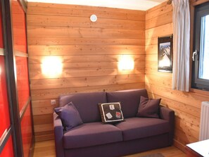 Ein Holzblockhaus-Innenraum mit einem violetten Sofa, zwei Wandleuchten und einem Fenster mit Vorhängen.