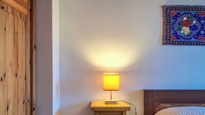 A wooden bedside table with a lamp, a bed with a white textured blanket, and a decorative wall hanging. - Dolce Casa - Residence La Montanara (Camigliatello Silano)