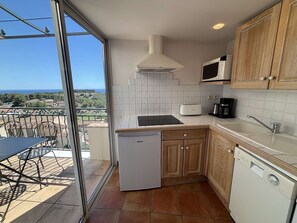 A compact kitchen with a dishwasher, a microwave, and a sink. There's a balcony with a table and chairs, and a view of the sea. - Apartment sea view - 6 guests (Saint-Cyr-sur-Mer)