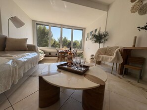 Ein modernes Wohnzimmer mit Sofa, Couchtisch, Essbereich und großem Fenster mit Blick ins Freie.