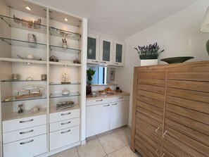 Een keuken met witte kasten, glazen planken en een houten kast.