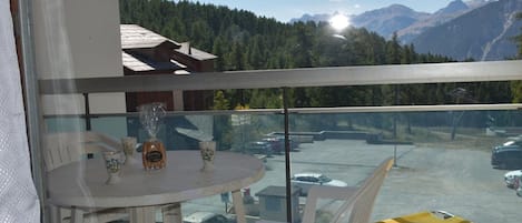 A balcony with a table and chairs, overlooking a parking area and mountains.