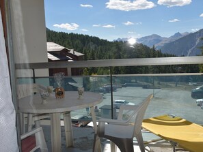 A balcony with a table and chairs, overlooking a parking area and mountains. - Studio at the foot of the slopes - 4 guests (Montgenèvre)