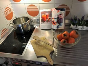 A kitchen with a stove, a pot, a bowl of tomatoes, a wooden cutting board, and a magazine on the counter. - Cozy central apartment - 5 guests (Montgenèvre)