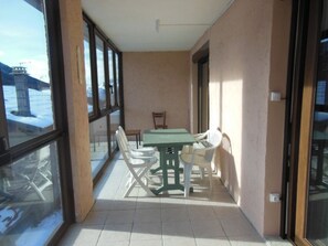 A balcony with a table and chairs, large windows, and a view of snow outside. - Cozy central apartment - 5 guests (Montgenèvre)
