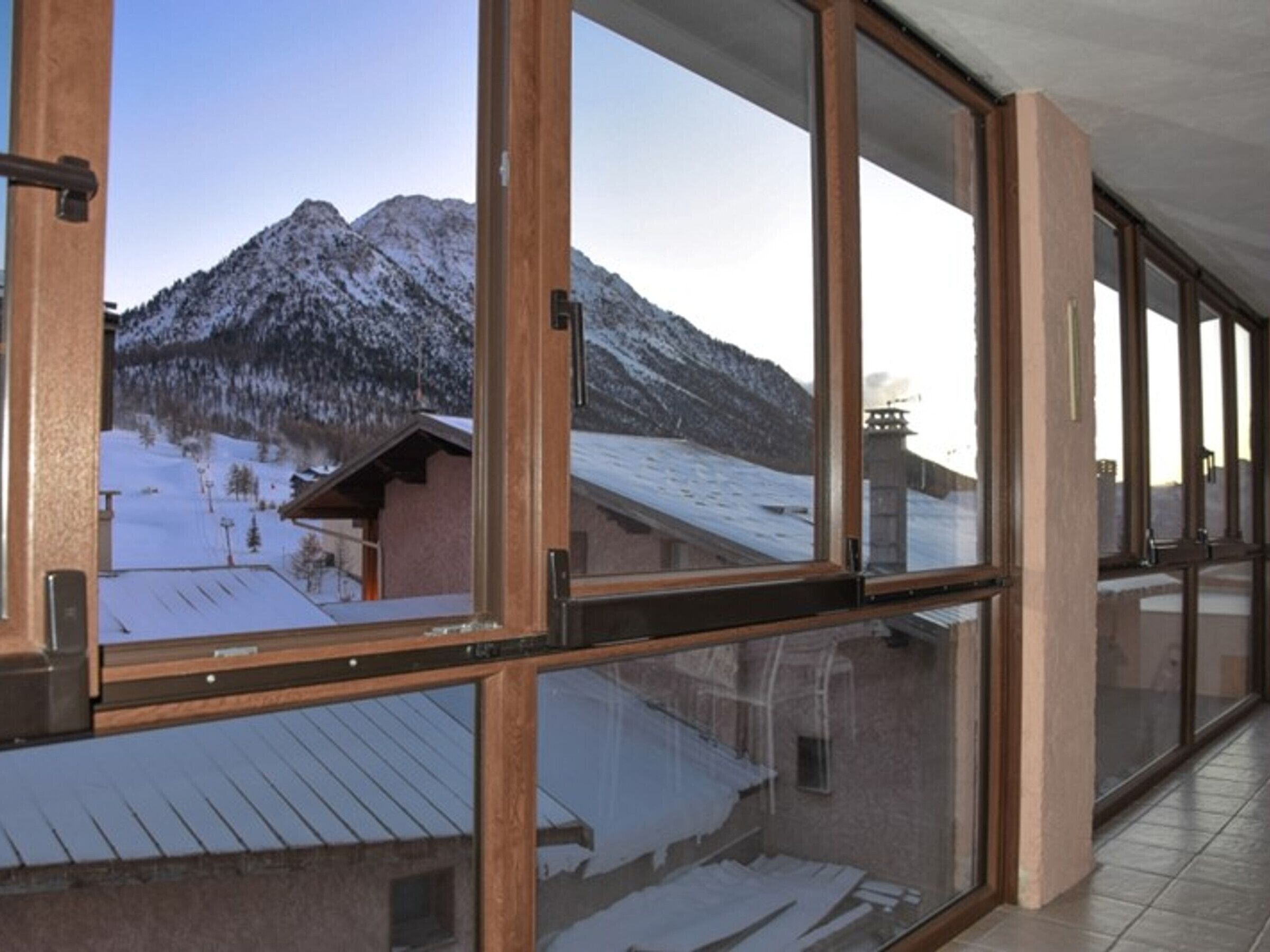 A corridor with large windows offering a view of a snowy mountain landscape.