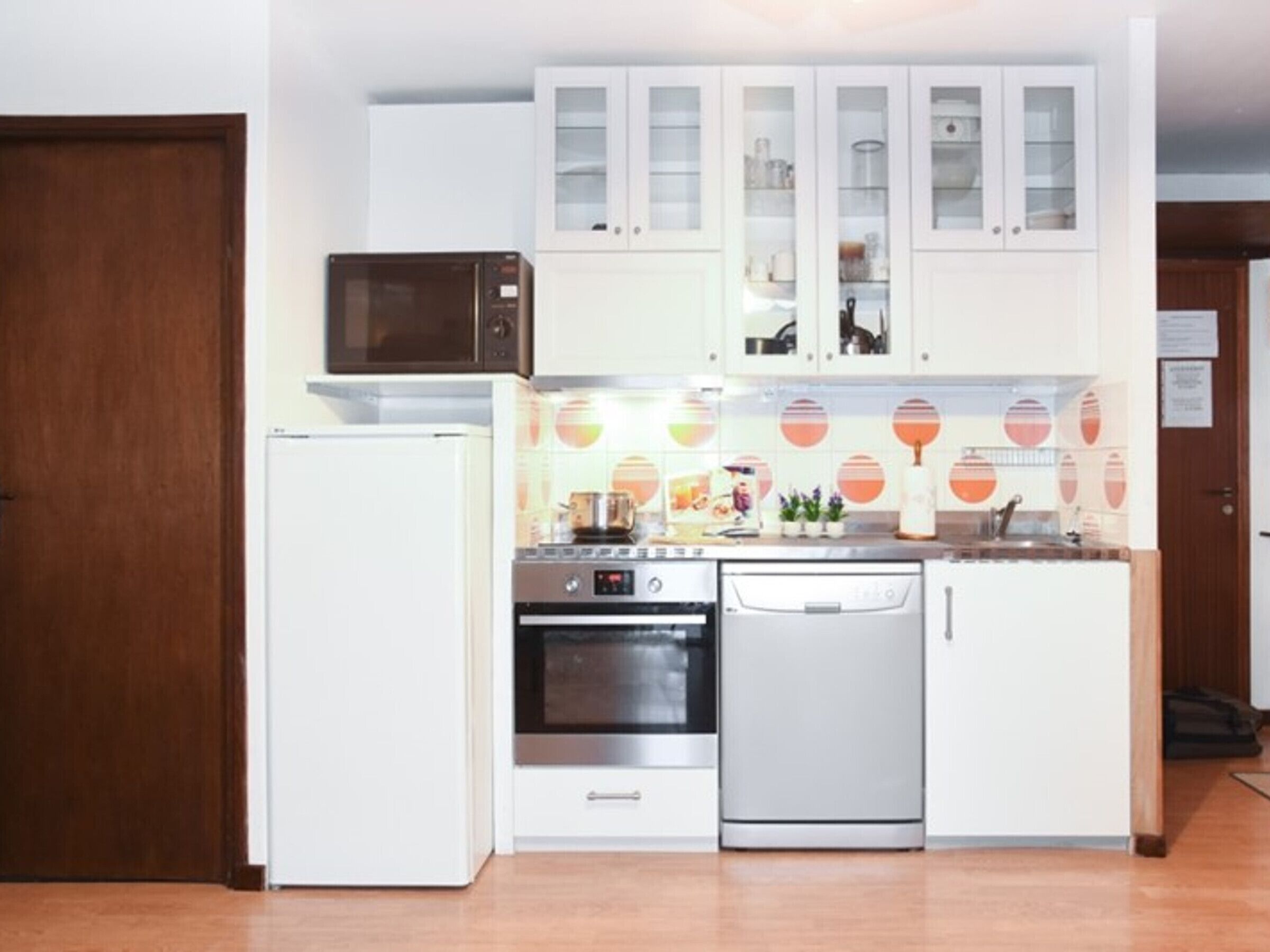 A compact kitchen with white cabinets, a microwave, a refrigerator, an oven, and a dishwasher.