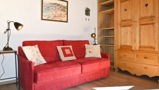 A red sofa with patterned cushions, a wooden cabinet, and a framed picture on the wall. - Studio with parking, pets OK, mountain view (Montgenèvre)