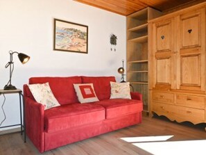 A red sofa with patterned cushions, a wooden cabinet, and a framed picture on the wall. - Studio with parking, pets OK, mountain view (Montgenèvre)