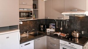 A modern kitchen with a built-in dishwasher, microwave, stove, and oven. There are hanging utensils and a coffee maker on the countertop. - Studio with parking, pets OK, mountain view (Montgenèvre)