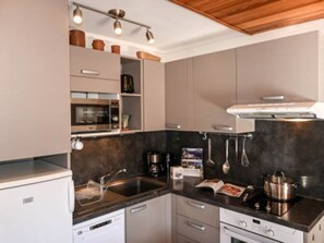 Eine moderne Küche mit Einbaugeschirrspüler, Mikrowelle, Herd und Backofen. Auf der Arbeitsfläche befinden sich hängende Küchenutensilien und eine Kaffeemaschine.