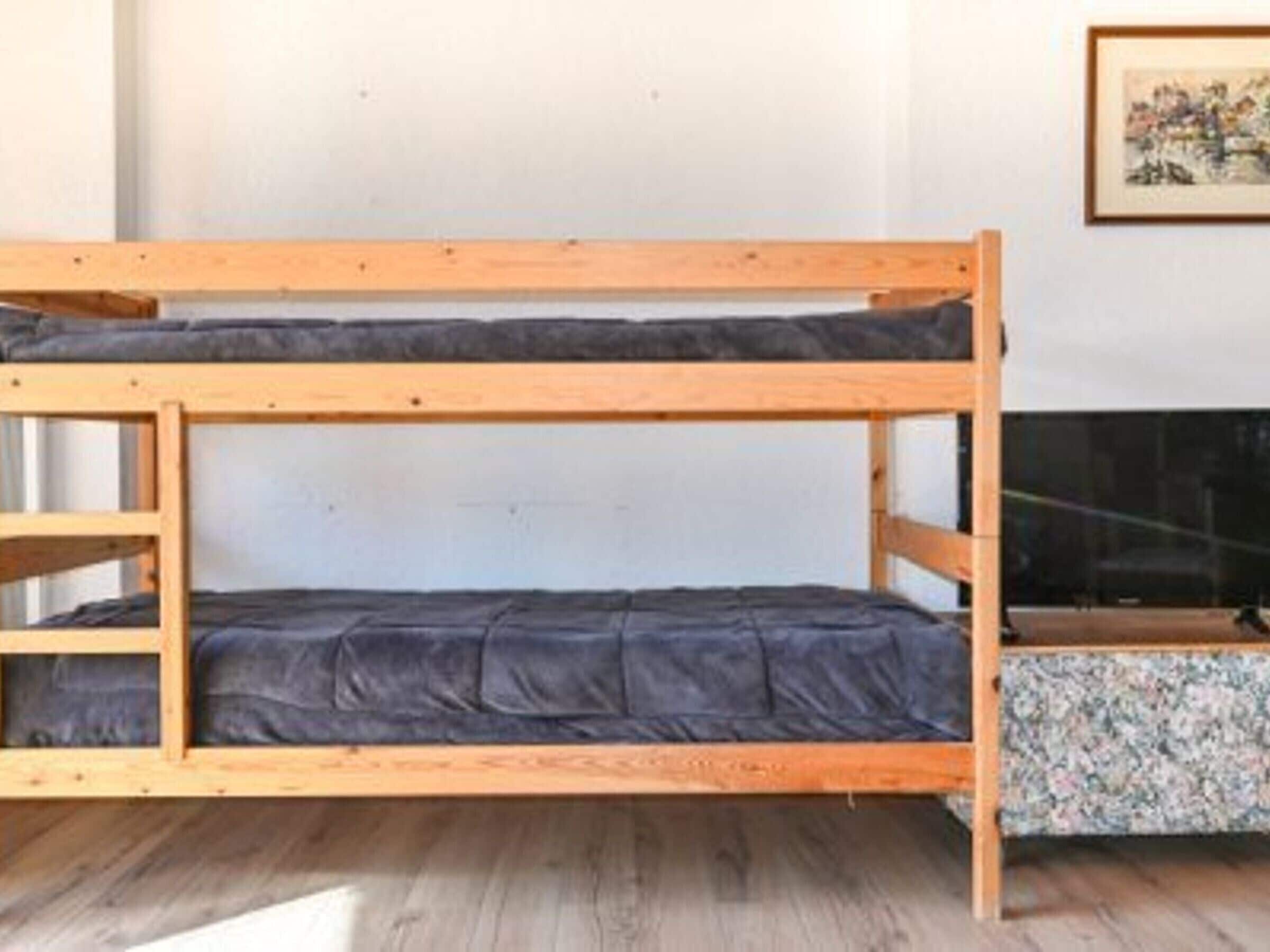 A bunk bed with a lower bunk and a mattress, a wooden headboard, and a framed picture on the wall.