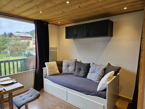 Ein gemütliches Zimmer mit einer eingebauten Schlafcouch, einem kleinen Tisch und Blick auf einen Garten sowie Häuser.