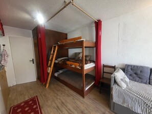 Ein Stockbett mit einer Stehle, ein kleiner Tisch und ein Sofa in einem Zimmer mit Holzboden und weißen Wänden.
