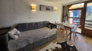 A modern living room with a sofa, dining table, and chairs. There is a large window with a view of trees and a mountain. - Studio in the village center with wifi - 4 guests (Montgenèvre)