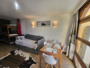 Ein gemütliches Zimmer mit Etagenbett, einer Couch, einem Esstisch mit Stühlen und einem Kuhfellteppich.