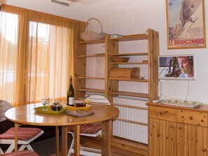 A dining area with a wooden table, chairs, a wine bottle, and a poster on the wall. - Studio in Montgenèvre center - 3 guests (Montgenèvre)