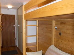 A wooden room with a bed, a door, and a wall-mounted lamp. - Studio in Montgenèvre center - 3 guests (Montgenèvre)