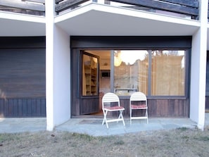 Une maison moderne dotée d’une grande porte-fenêtre coulissante qui donne sur un patio aménagé avec deux chaises blanches.