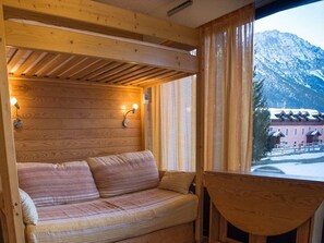 Une cabane en bois avec un canapé, deux lampes fixées au mur et une vue sur une montagne.