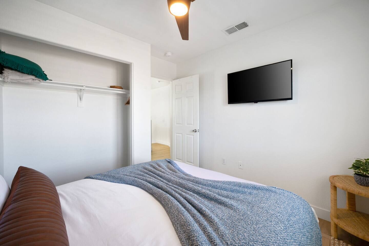 A bedroom with a bed, a TV mounted on the wall, a wardrobe, and a small plant on a shelf.
