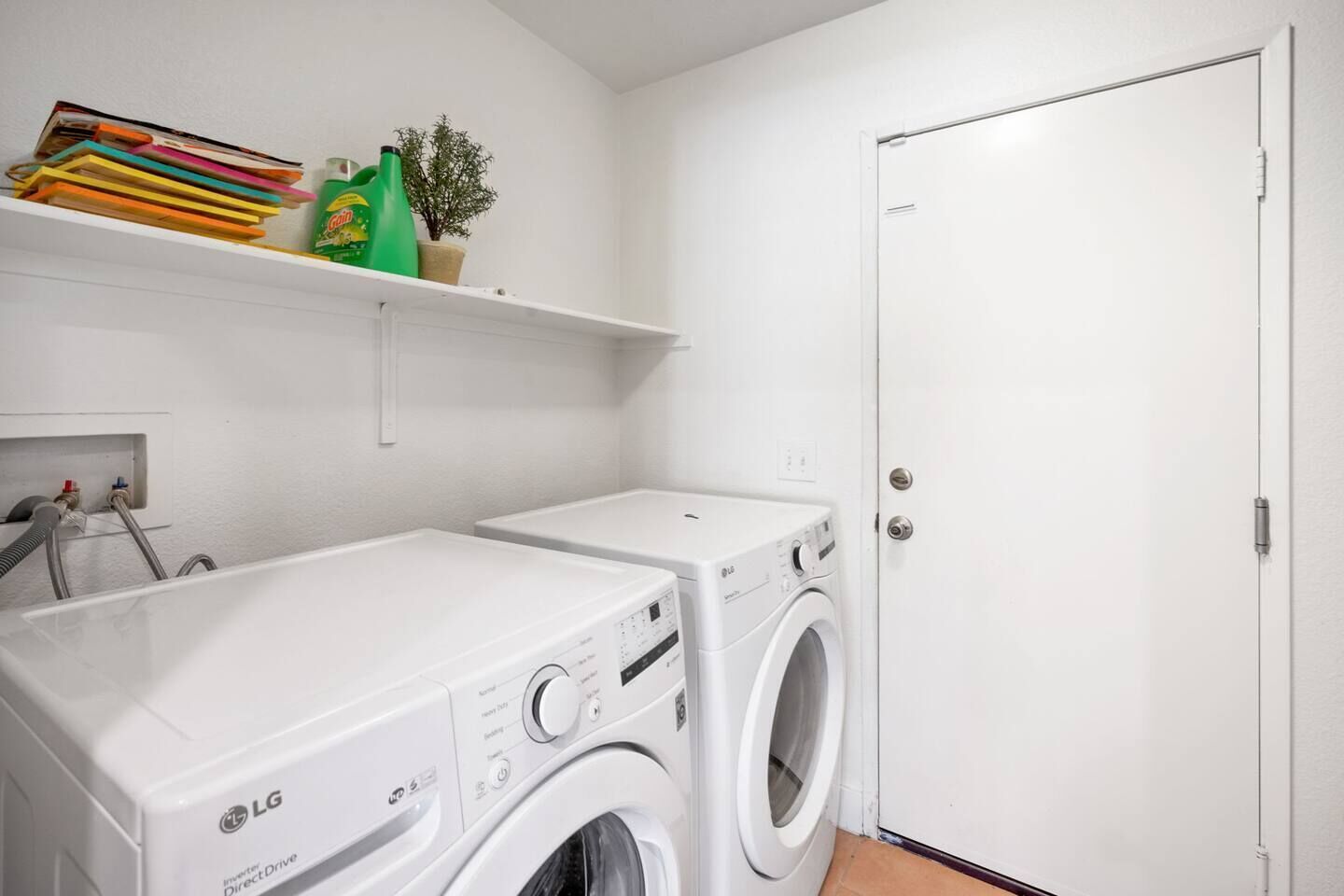 A laundry room with two white LG washing machines, a shelf with cleaning supplies, and a potted plant.
