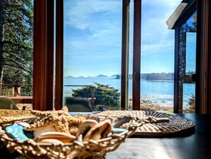 A view from a room with large windows overlooking a body of water and distant land, with woven mats on the windowsill. - Charming Waterfront Sea Cottage with Private Beach near Bar Harbor, Hancock Maine (Hancock)