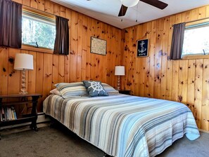 A wooden-paneled room with a bed, two bedside lamps, a map on the wall, and a nautical-themed pillow. - Secluded Oceanfront Cottage with Wrap-Around Deck near Acadia National Park, Sullivan, Maine (Sullivan)