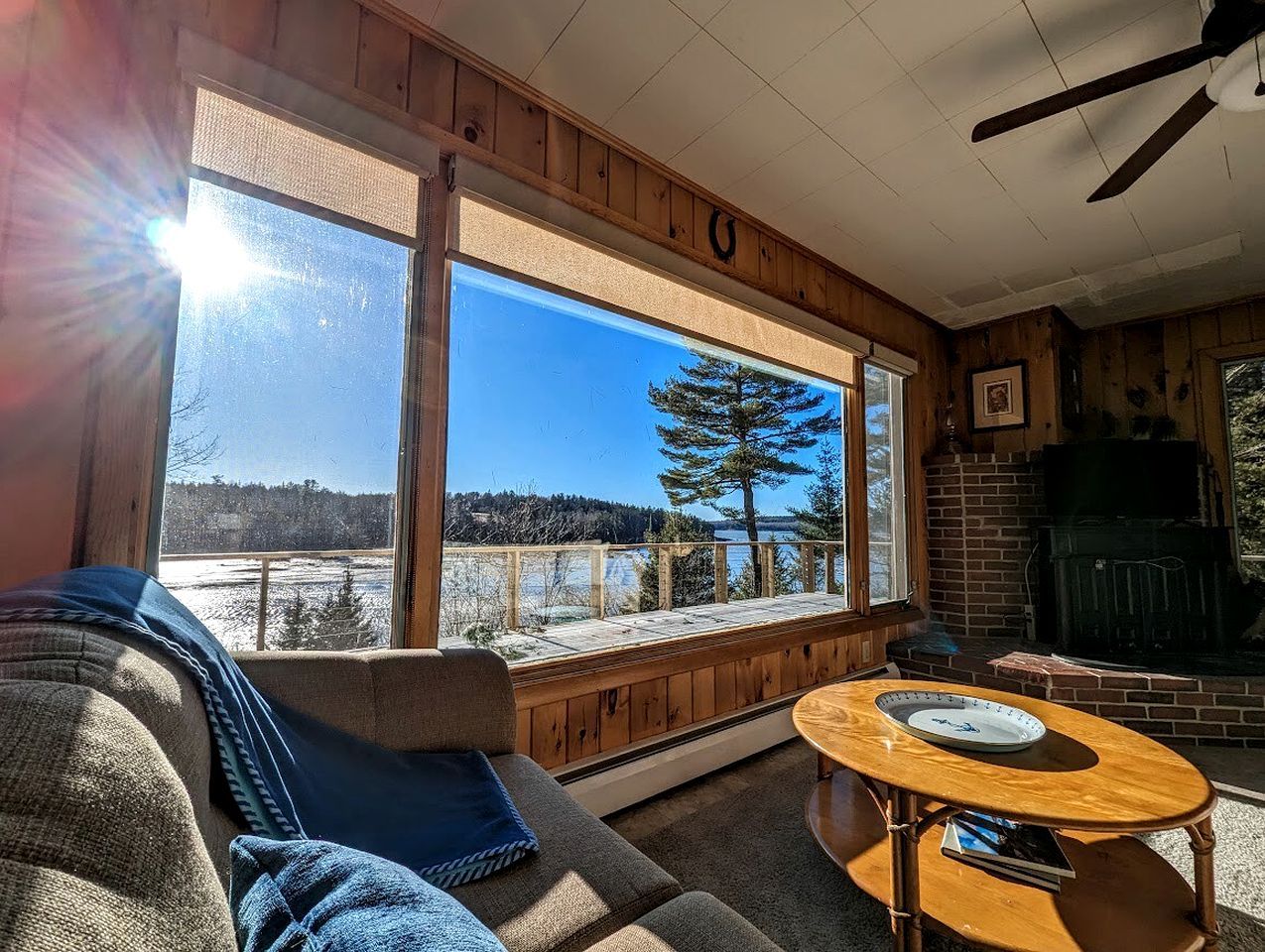 A cozy living room with a large window, a fireplace, and a wooden ceiling.