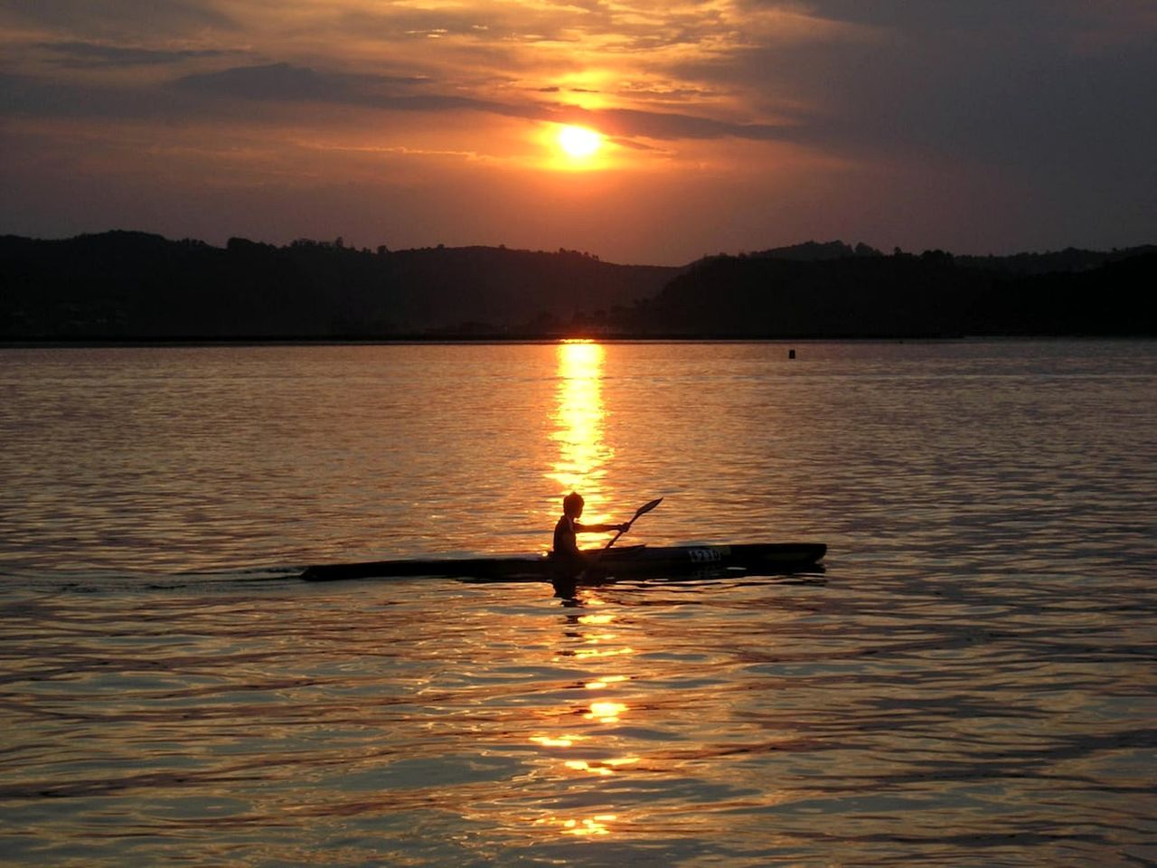 A person rowing a boat on a calm body of water during sunset.
