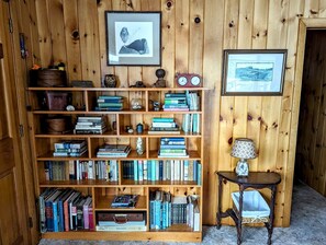 Une bibliothèque en bois remplie de livres, un tableau encadré accroché au mur et une petite table avec une lampe.