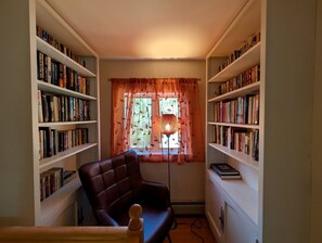 Ein Zimmer mit Bücherregal, einem Sessel und einem fenster mit Vorhängen.