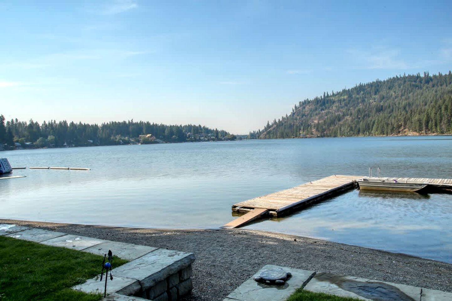 Un lac paisible, avec une jetée en bois qui s’avance sur l’eau, entouré de collines boisées.