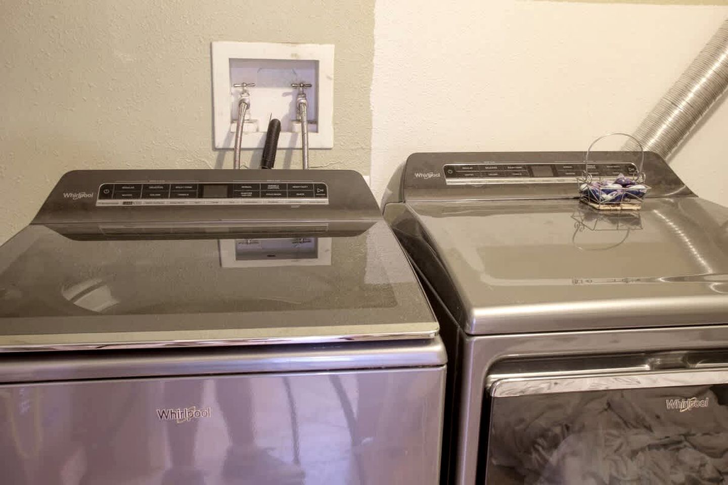 Dos lavadoras Whirlpool una al lado de la otra, con un enchufe y una manguera de agua al fondo.
