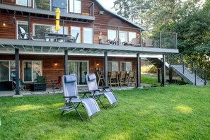 Ein zweistöckiges Holzhaus mit einer überdachten Veranda, Sitzgelegenheiten im Freien und einer Treppe, die zum oberen Stockwerk führt.