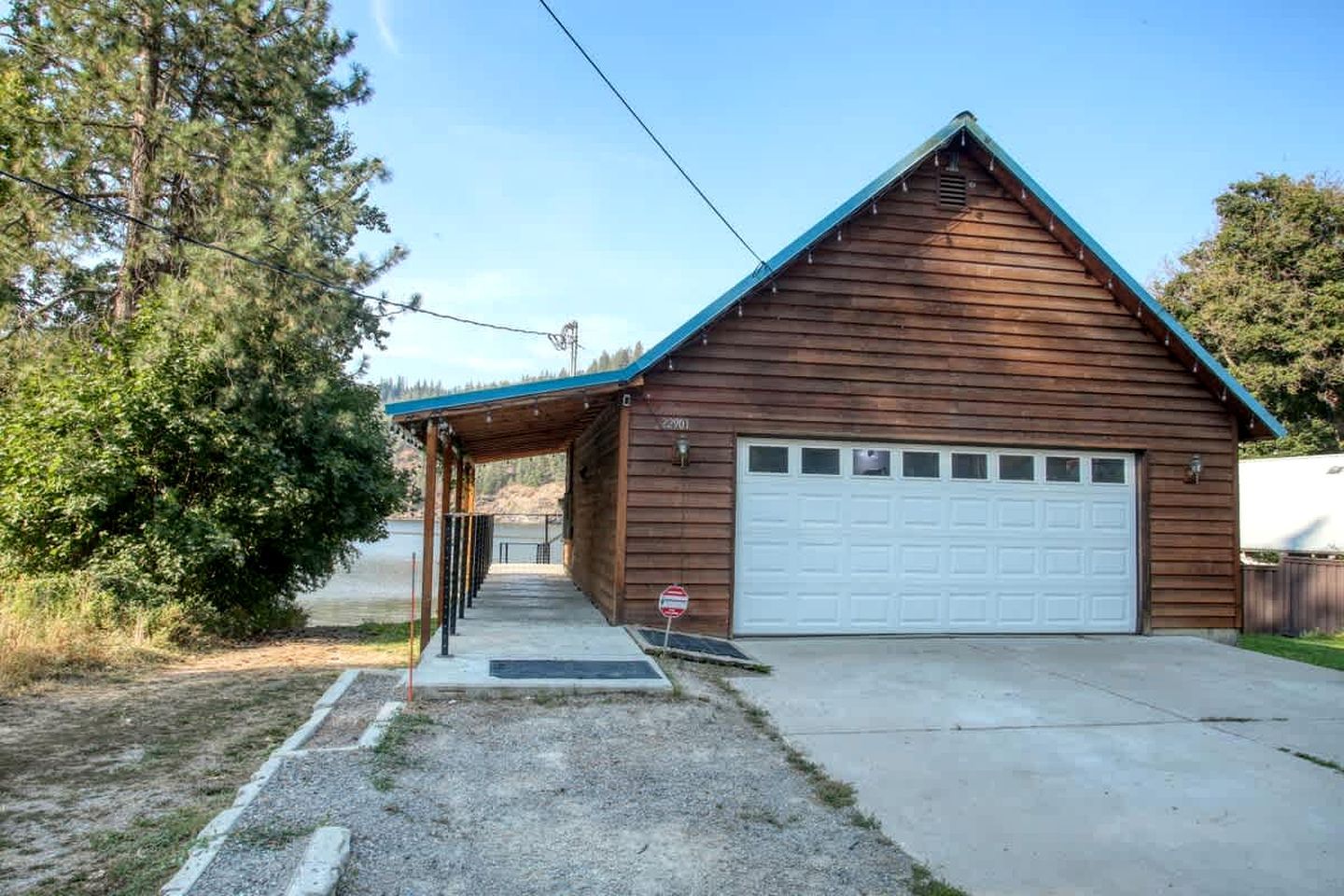 Une cabane en bois avec un garage, une véranda et une allée gravillonnée.