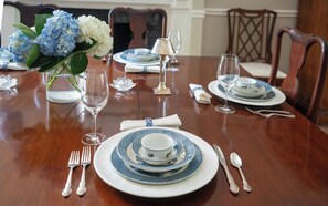 A dining table set with blue and white plates, silverware, and a vase with blue and white flowers.