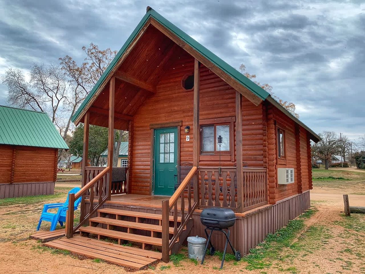 Eine Holzhütte mit Veranda, einer grünen Tür und einem Grill vor der Tür.