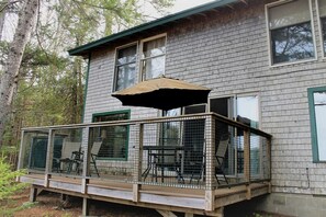 Eine Holzterrasse mit überdachter Sitzgruppe, umgeben von einem Metallzaun, an ein Haus mit vielen Fenstern angebaut.