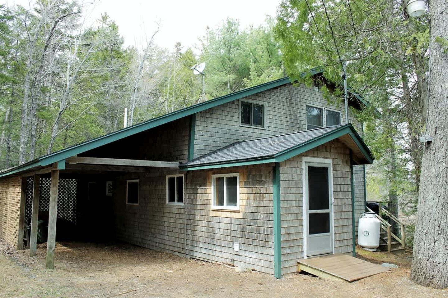 A two-story cabin with a covered porch, a small attached garage, and a satellite dish.