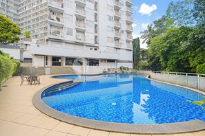 Una piscina con bordo piastrellato, circondata da una recinzione, adiacente a un edificio residenziale a più piani.