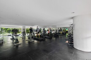 Un gimnasio con varios equipos de ejercicio, un pilar grande y vistas a zonas verdes.