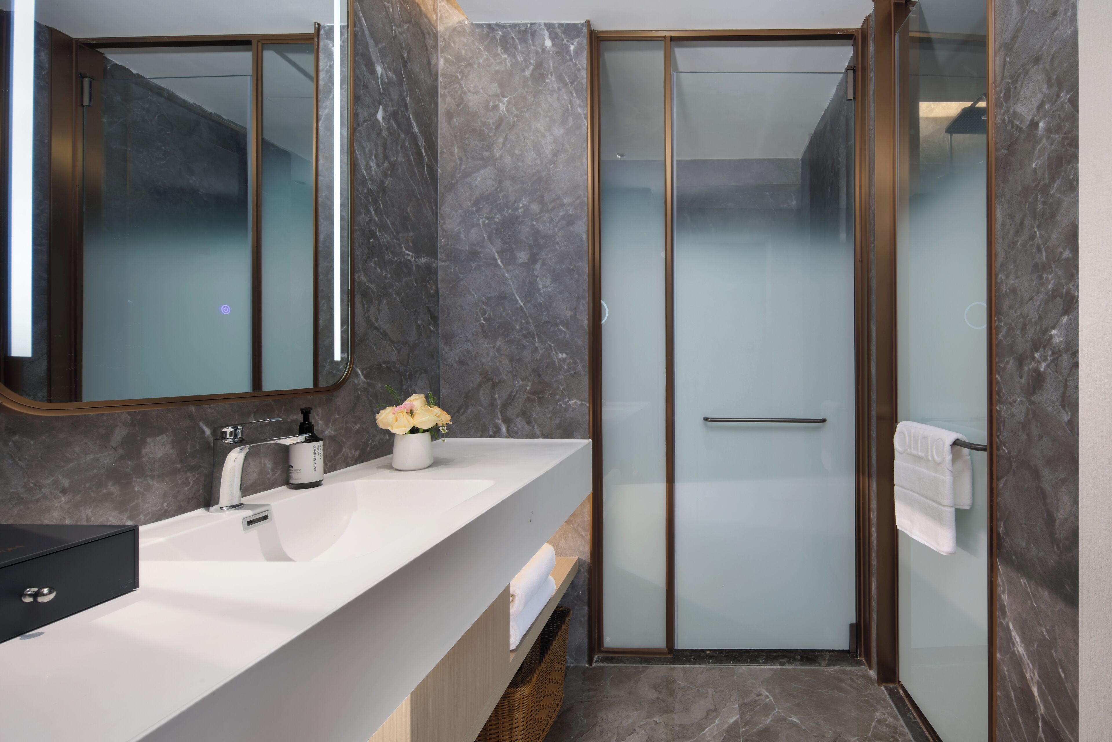 A modern bathroom with a marble countertop, a glass shower enclosure, and a wooden floor.