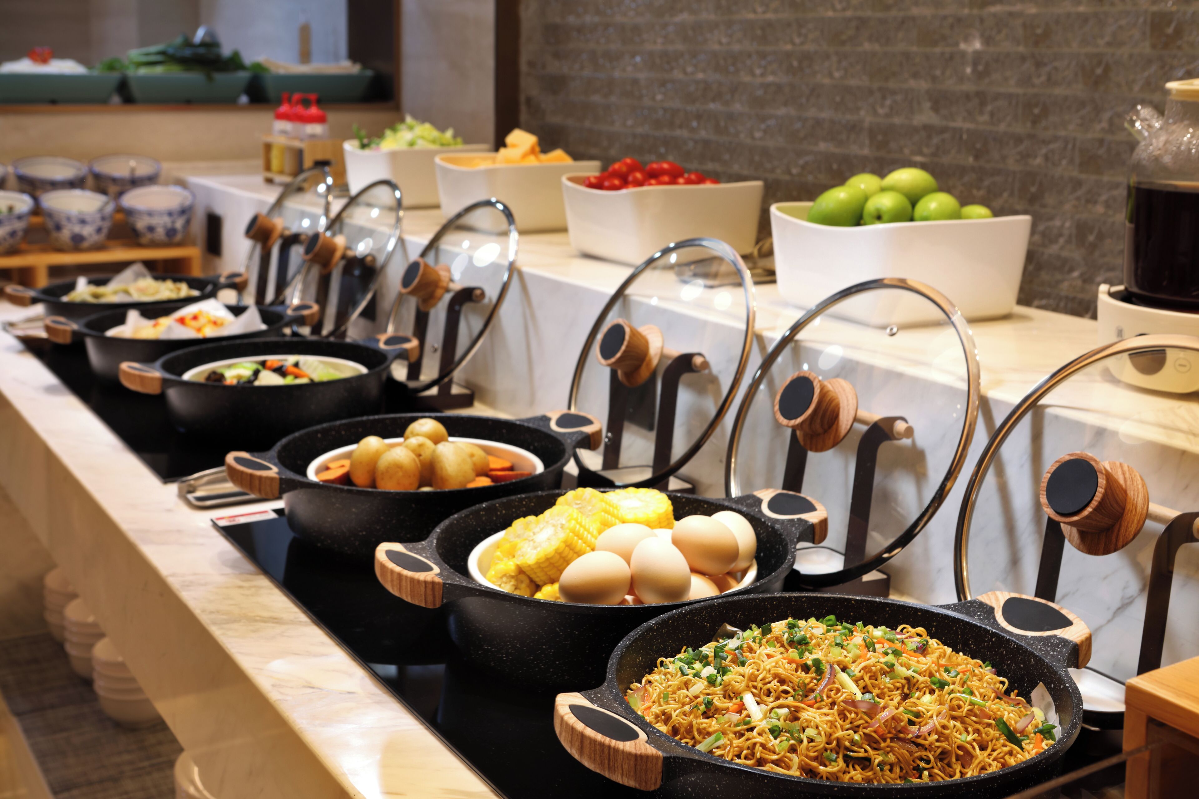 Buffet com diversos alimentos, incluindo vegetais, frutas e um prato de macarrão.