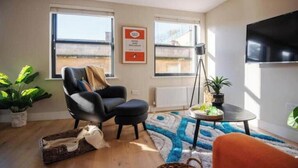 Una sala de estar con un sillón negro, una mesita redonda con una planta, una lámpara de pie y un ventanal grande.