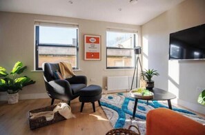 Ein Wohnzimmer mit einem schwarzen Sessel, einem kleinen runden Tisch mit Pflanze, einer Stehlampe und einem großen Fenster.