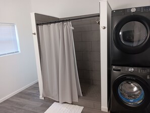 A laundry room with a washing machine, a shower with a curtain, and a window with blinds. - The Longview lake house (Coldwater)
